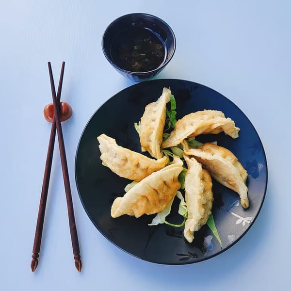 Chinnie's Kitchen fried dumplings on a black plate with a side of dipping sauce and chopsticks.