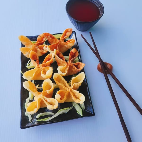 Crab rangoons on a black plate with a side of red dipping sauce and chopsticks.