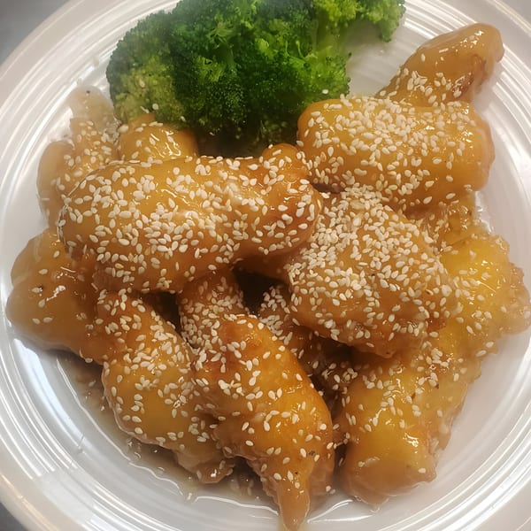 Chinnie's Kitchen's sesame chicken with a side of steamed broccoli on a white plate.