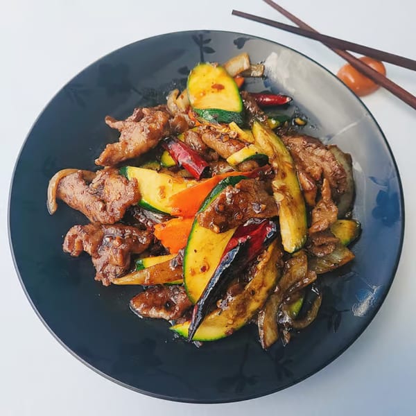 Chinnie's Kitchen's stir-fried beef with zucchini, carrots, and peppers on a dark plate with chopsticks.